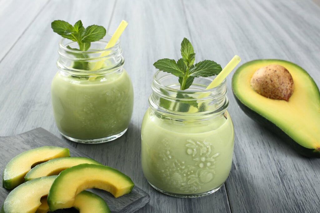 Dois copos com vitamina de abacate decorados com folhas de hortelã em cima de uma mesa