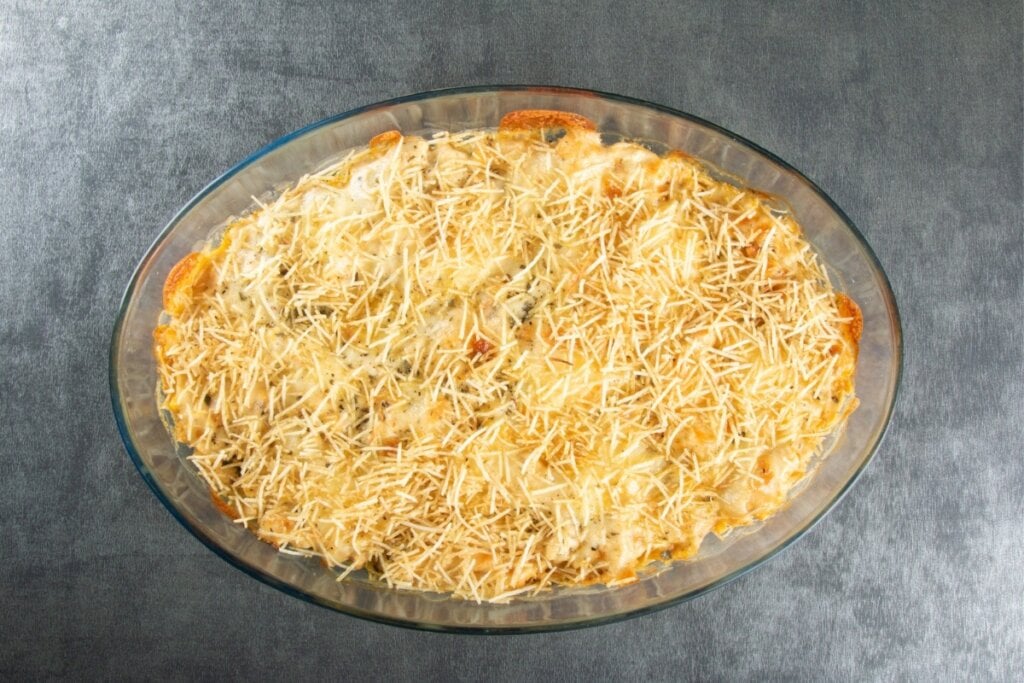 Travessa de vidro com fricassê polvilhado com batata-palha em cima de uma mesa cinza