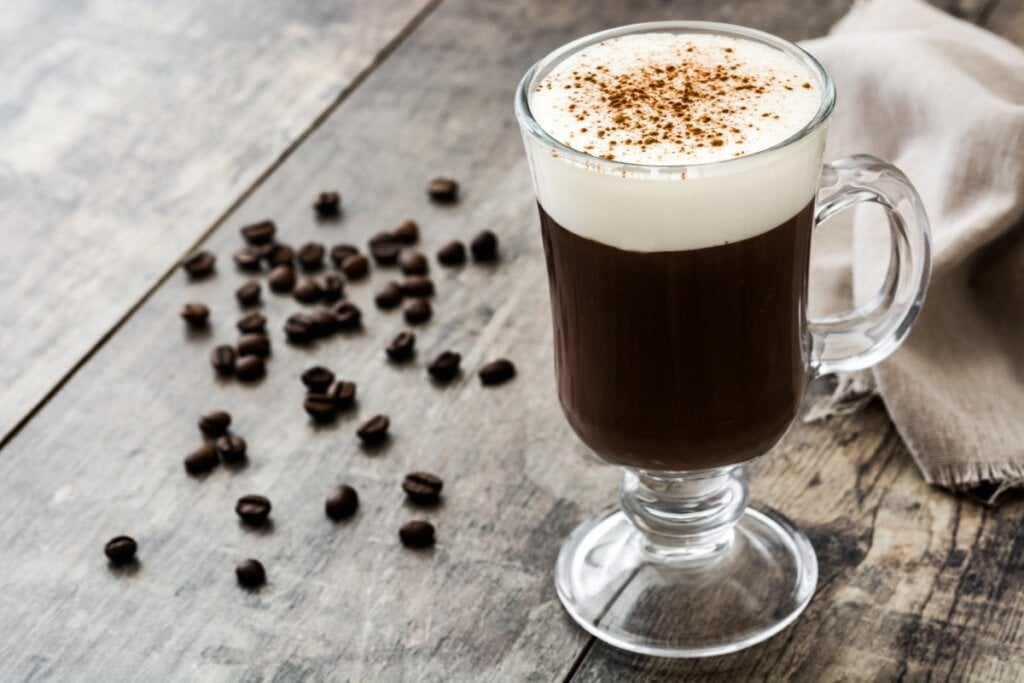 Irish coffee em uma caneca de vidro transparente em cima de uma mesa de madeira com grãos de café 