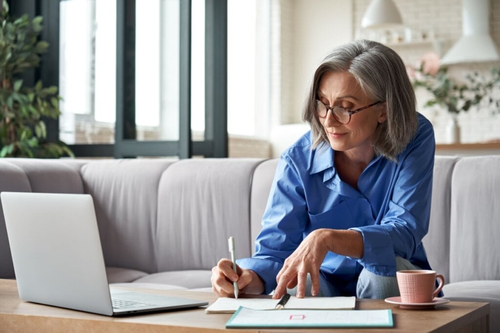 mulher escrevendo em papel em uma mesa com notebook