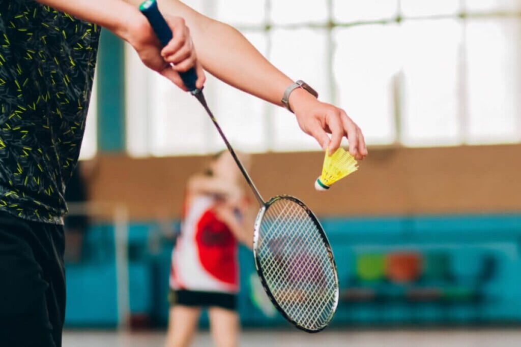 Pessoa segurando uma raquete de badminton e uma bola jogando em uma quadra 