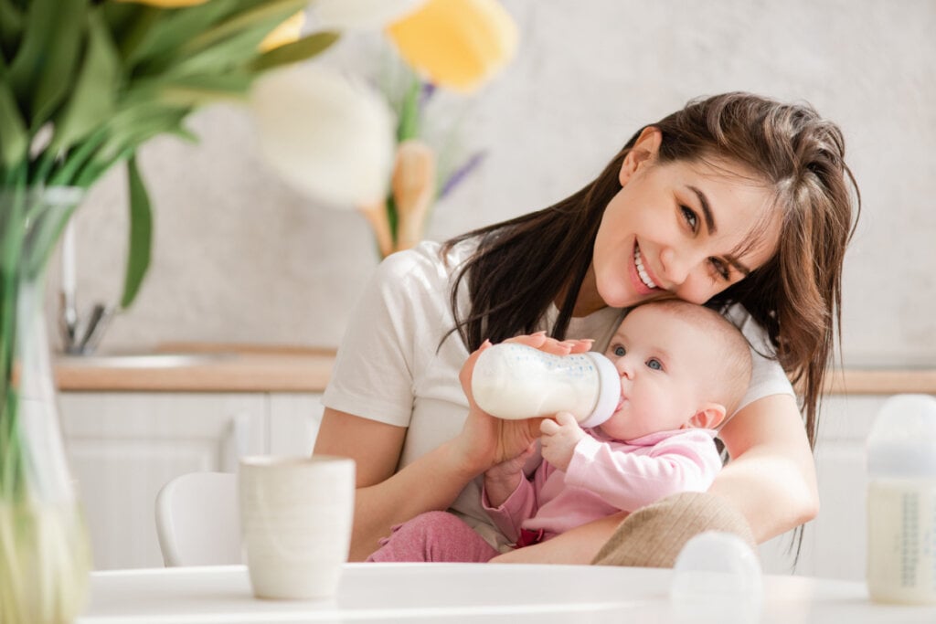 Mãe dando segurando mamadeira para bebê com roupa rosa