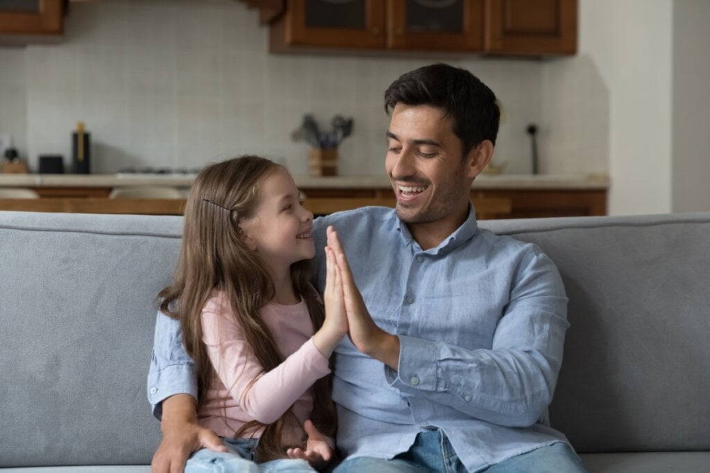 pai e filha sentados no sofá encostando as mãos em "high five"