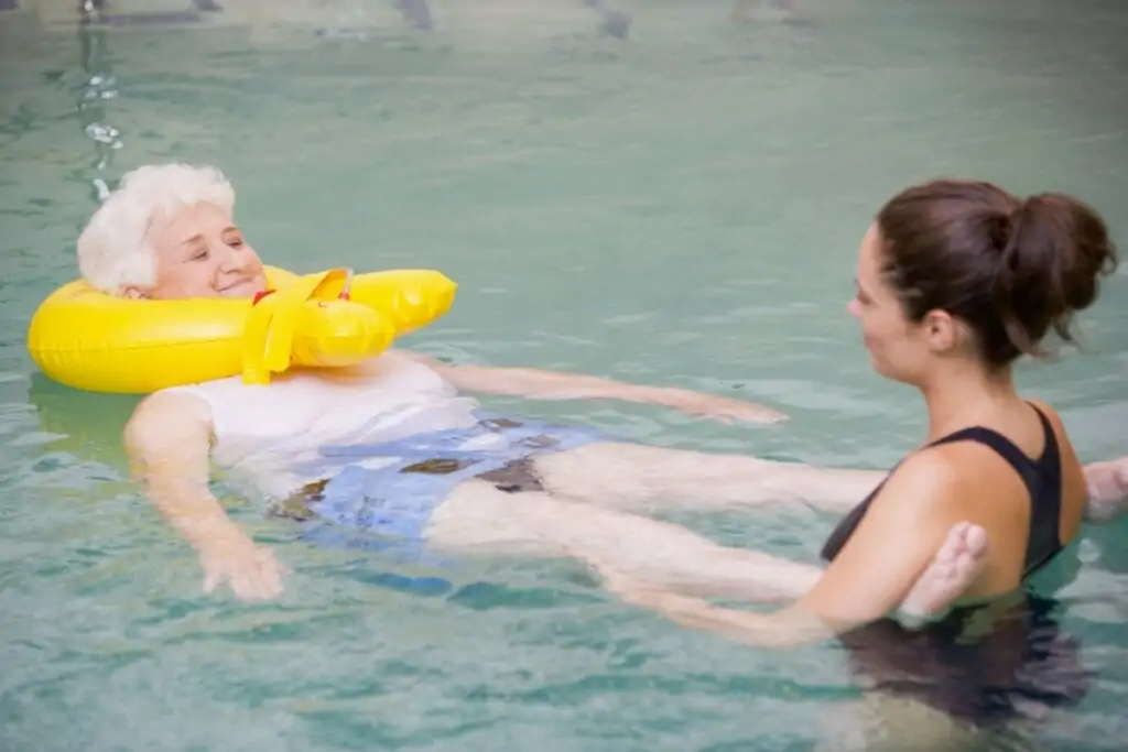 Instrutora ajudando uma idosa dentro de uma piscina 