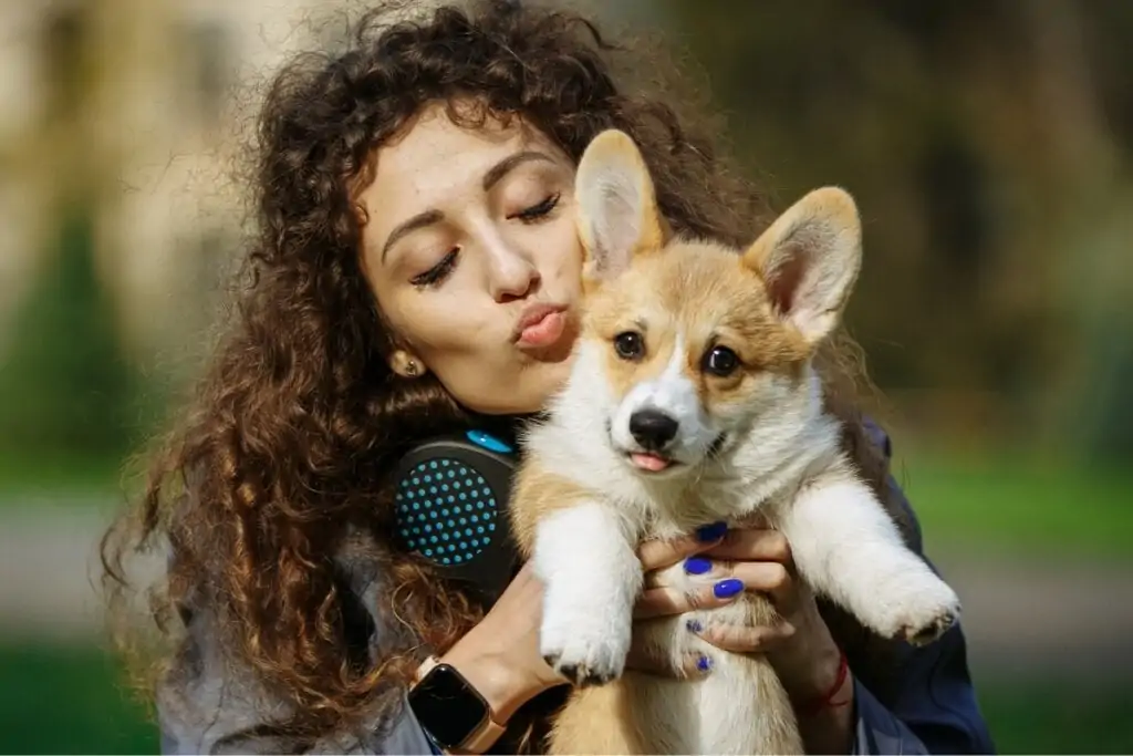 Mulher segurando e dando beijo em um cachorro com pelagem branca e dourada 