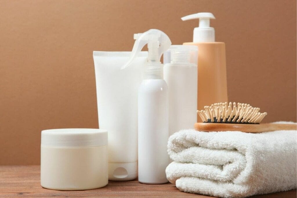 Potes de produtos spray e creme, escova de cabelo e uma toalha branca