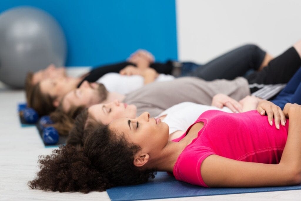 Mulheres deitadas em colchonetes fazendo exercício de respiração