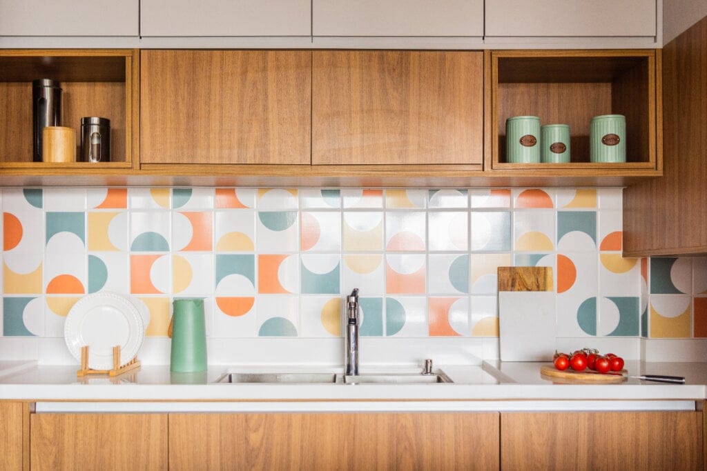 imagem de cozinha com armários de madeira e azulejo na parede em tons de verde, amarelo e laranja