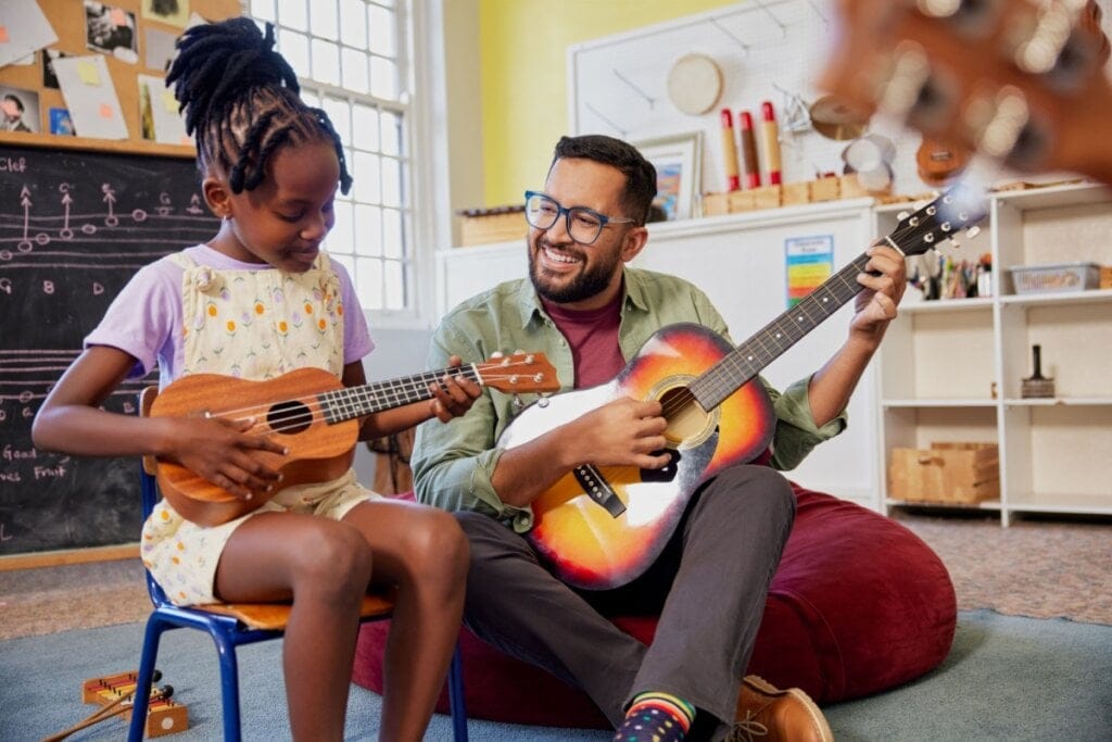 homem sentado no chão e menina em cadeira. eles estão tocando violão e sorrindo