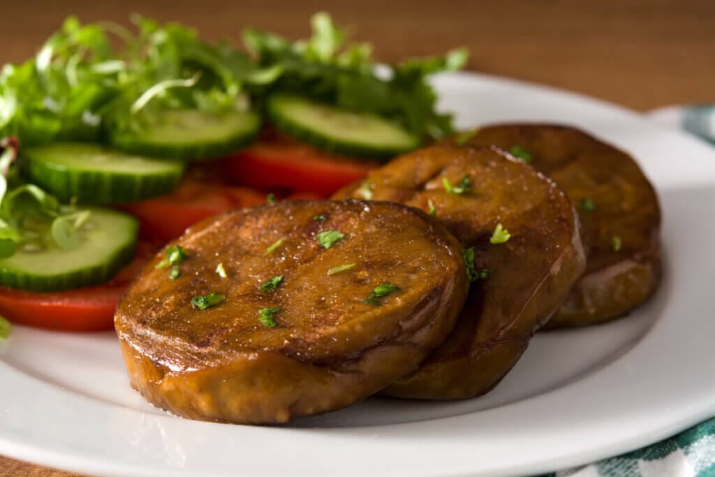Pedaços de carne seitan em um prato branco com pepino, tomate e alface