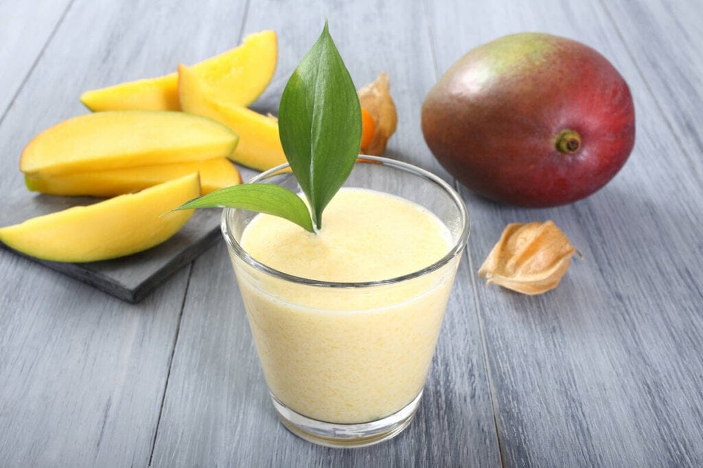 Copo de vidro com vitamina de manga decorado com folhas