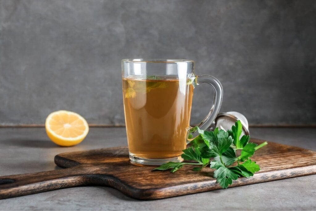 Caneca de vidro transparente com chá de salsa e limão em cima de uma tábua de madeira