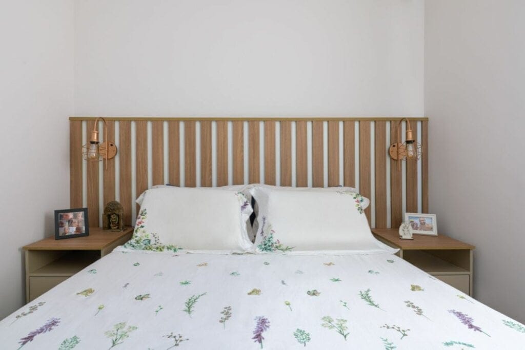 Cabeceira com madeira ripada atrás de uma cama com lençol branco