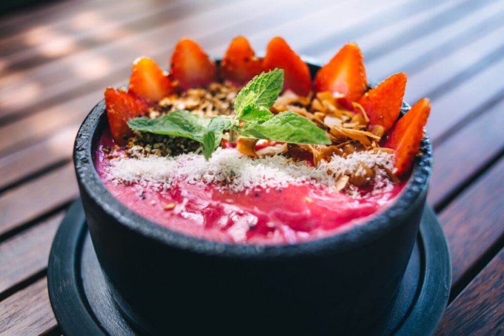 Recipiente preto com creme de pitaya, morangos, coco ralado e chips de coco