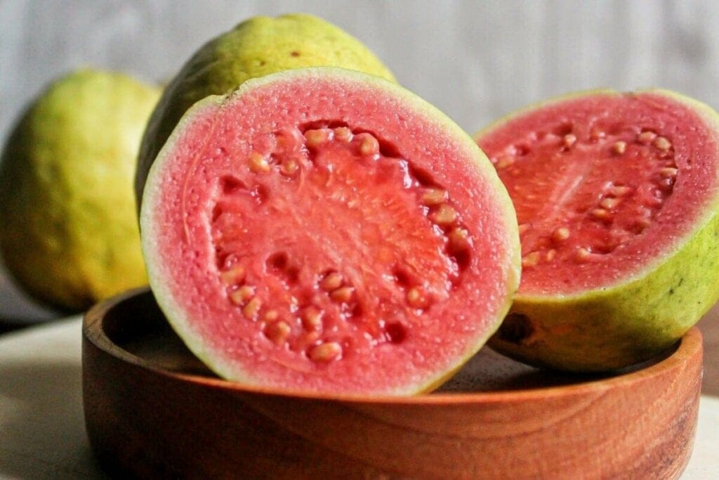 Goiaba cortada ao meio e atrás uma goiaba inteira em cima de pote de madeira