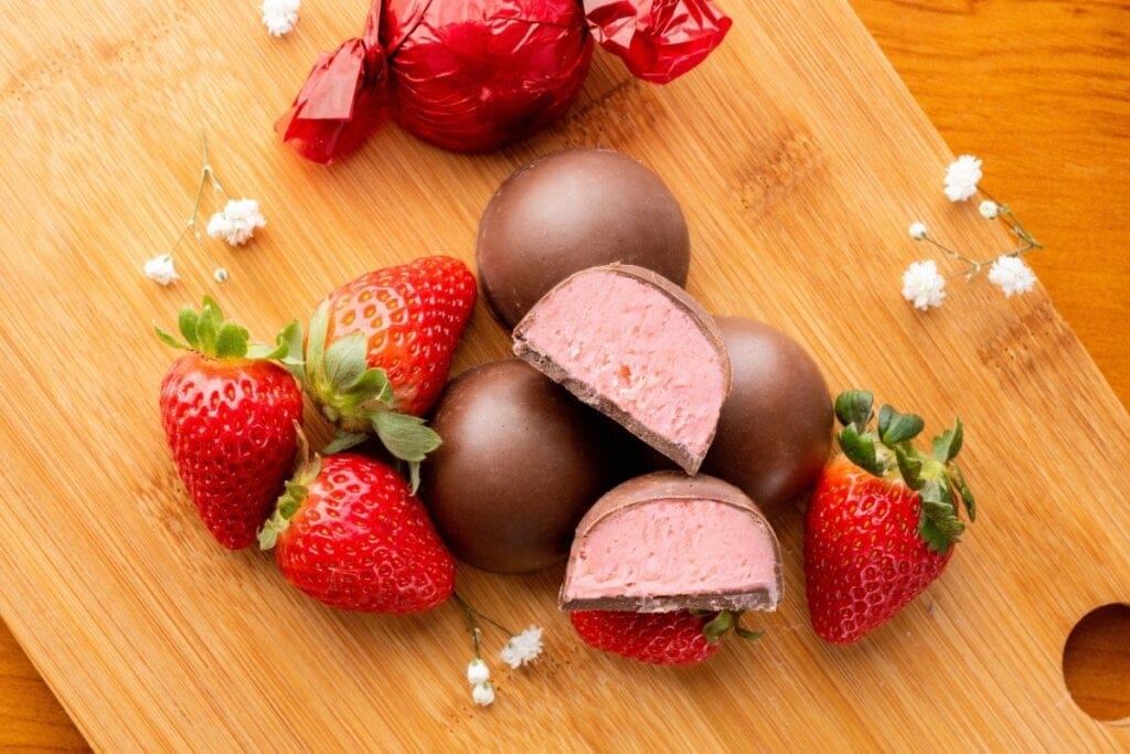 Trufas de morango em cima de uma mesa de madeira com morangos ao lado