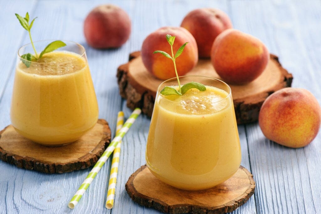 Dois copos de vitamina com pêssego e pêssegos ao fundo