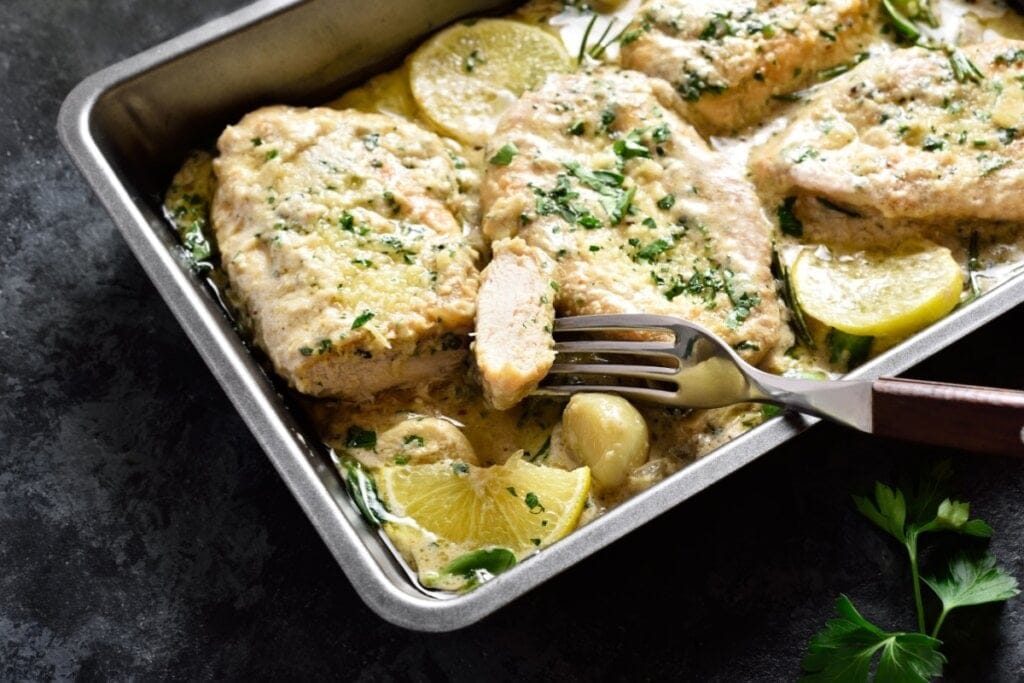 Assadeira com frango, molho, dentes de alho e rodelas de limão