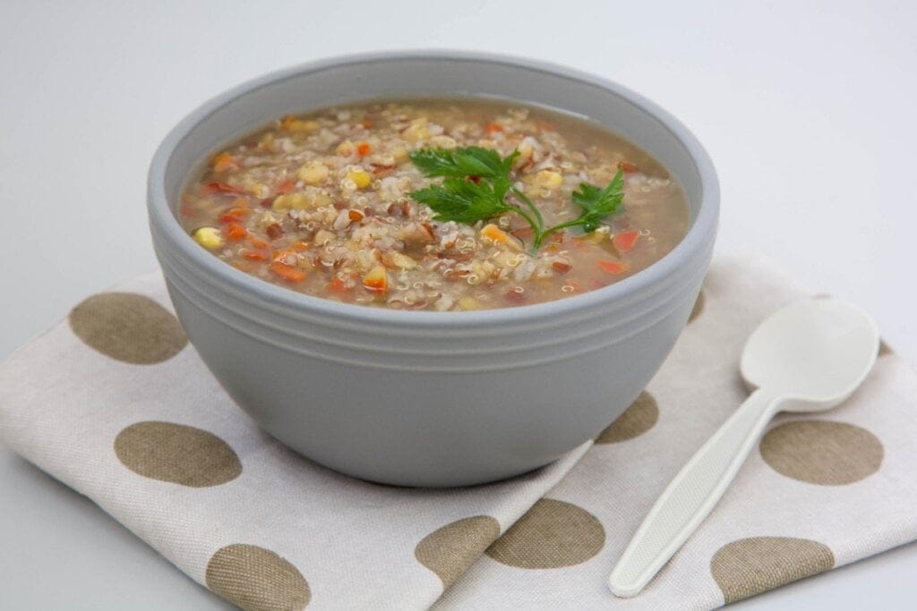 Recipiente cinza com sopa de lentilha com cenoura, milho-verde, arroz vermelho, lentilha e salsinha
