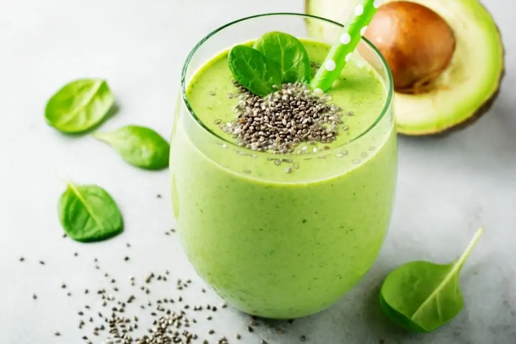 Copo de vidro com vitamina de abacate decorado com folhas de espinafre e sementes de chia