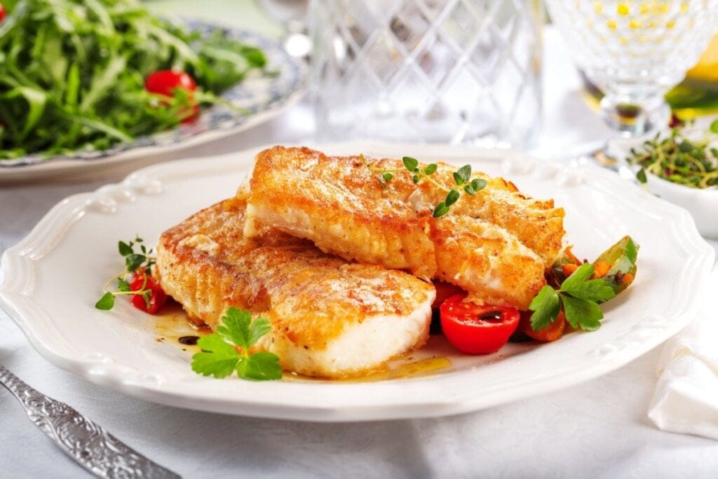 prato branco com dois filés de peixes grelhados com tomate-cereja e folhas de salsinha