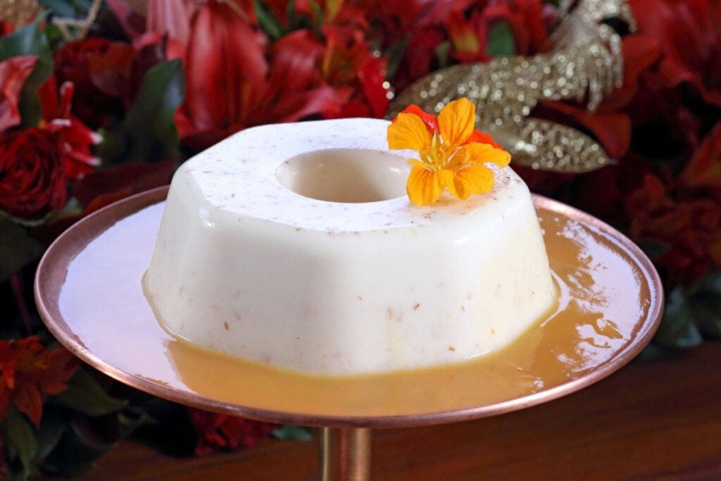 Pudim de coco com calda de caramelo e decorado com flores.