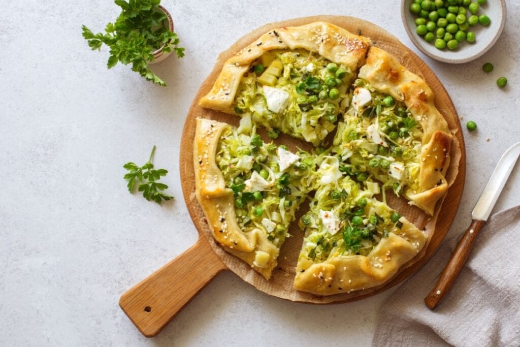 Torta aberta de repolho, ervilha e queijo feta fatiada em tábua redonda 