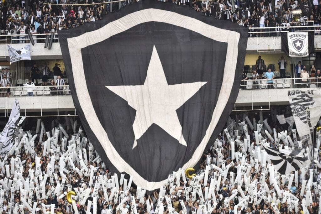 bandeira grande com brasão do botafogo estendida sobre arquibancada em estádio