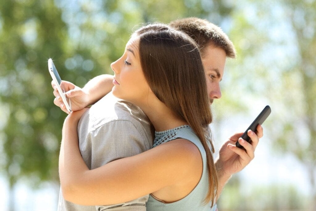 Casal abraçado e cada um mexendo em um celular