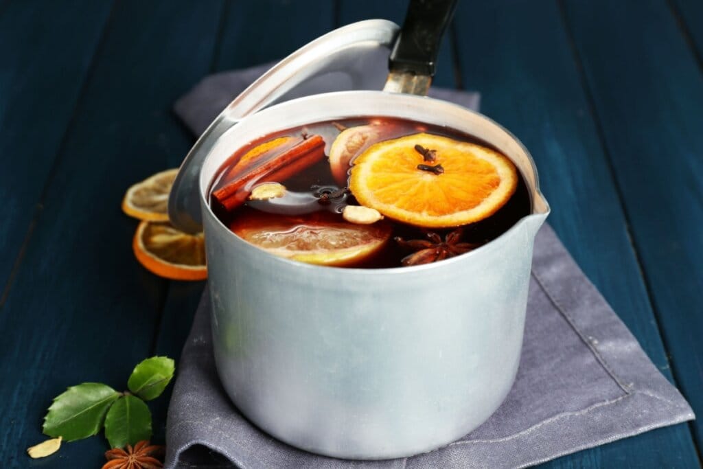 Panela metálica com bebida vermelha e rodelas de laranja, cravo, canela e anis em infusão