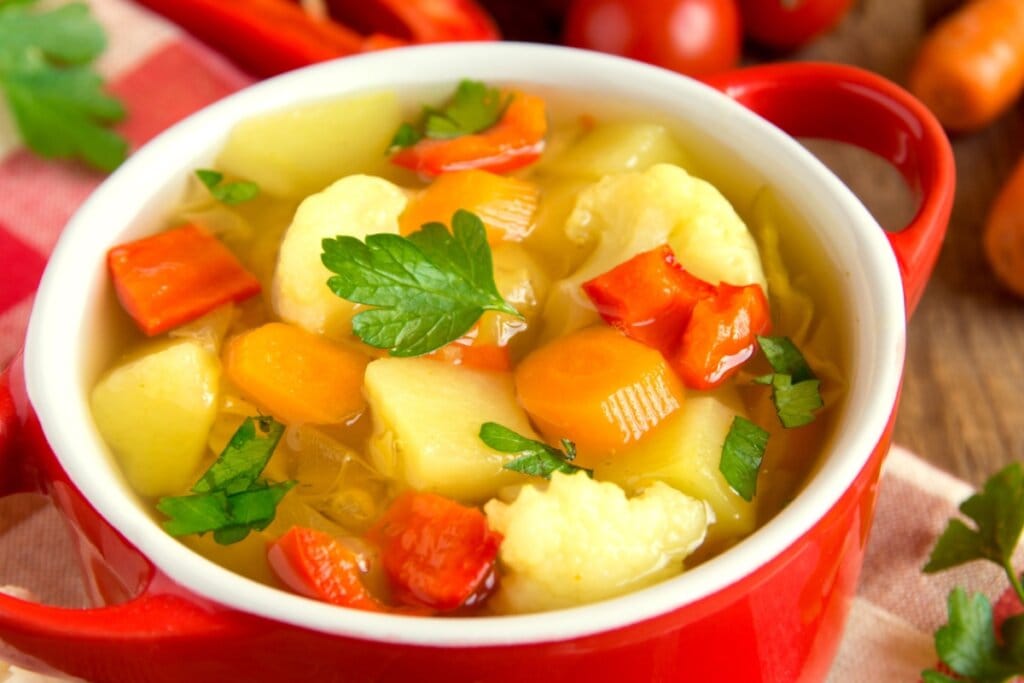 Panela vermelha com sopa de cenoura com batata, pimentão vermelho e couve-flor