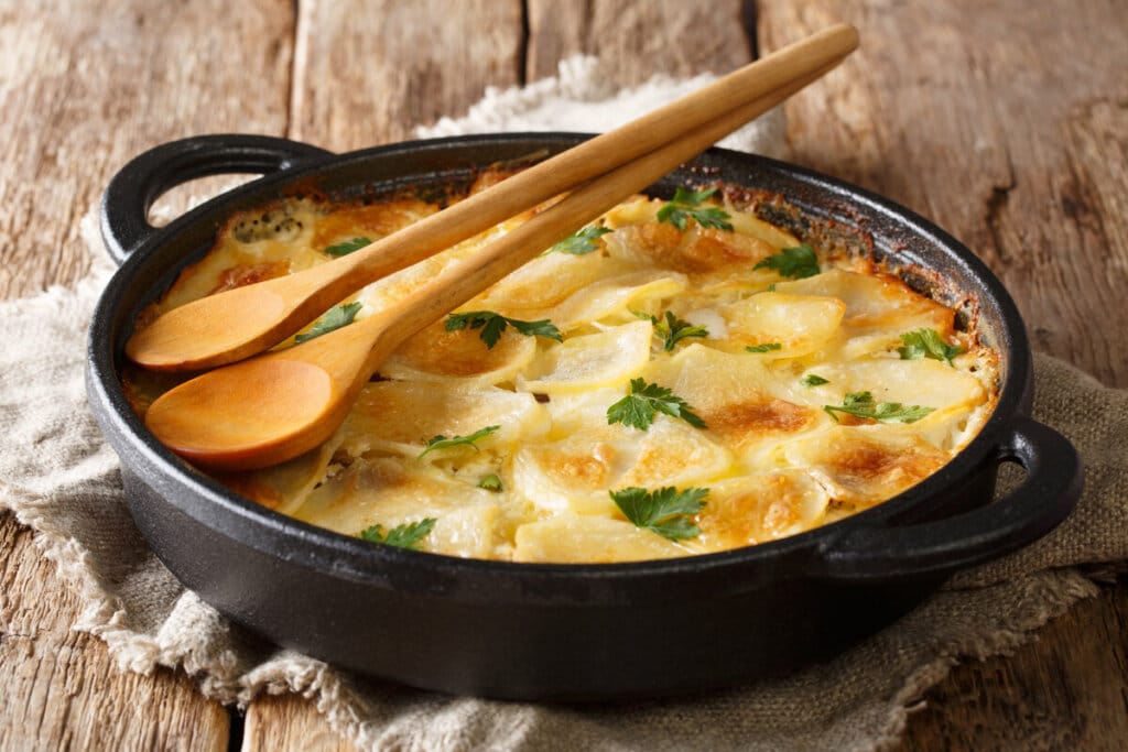Panela preta com batata gratinada polvilhada com folhas de coentro