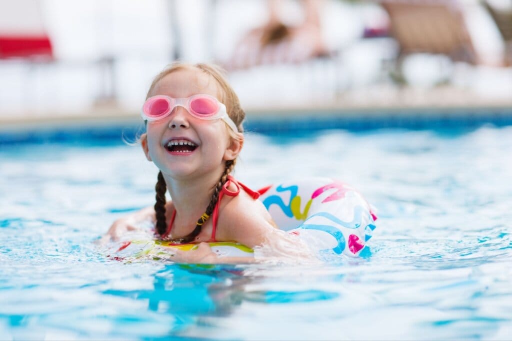 Criança brincando em piscina com boia e usando óculos de natação
