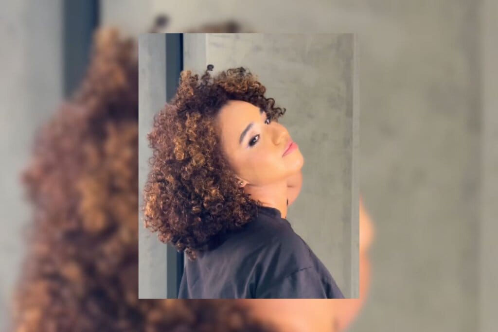 Mulher com cabelo cacheado com mechas em tom de chocolate posando para foto 