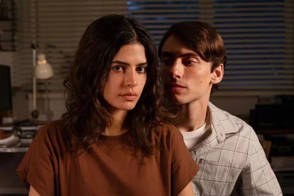 Protagonistas de Dias Perfeitos em uma sala de estar. A mulher está à frente, olhando para o lado, enquanto o homem permanece atrás dela, observando-a