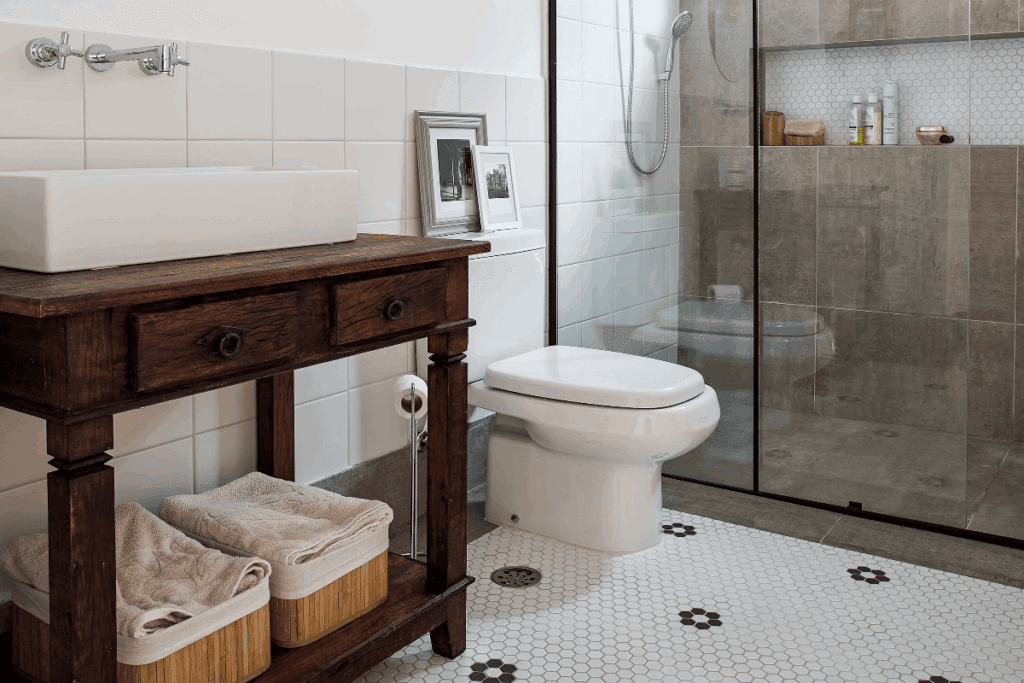 Banheiro com piso de pastilha branca com desenho de flores em preto e com móvel de madeira com cestos de utensílios e box 