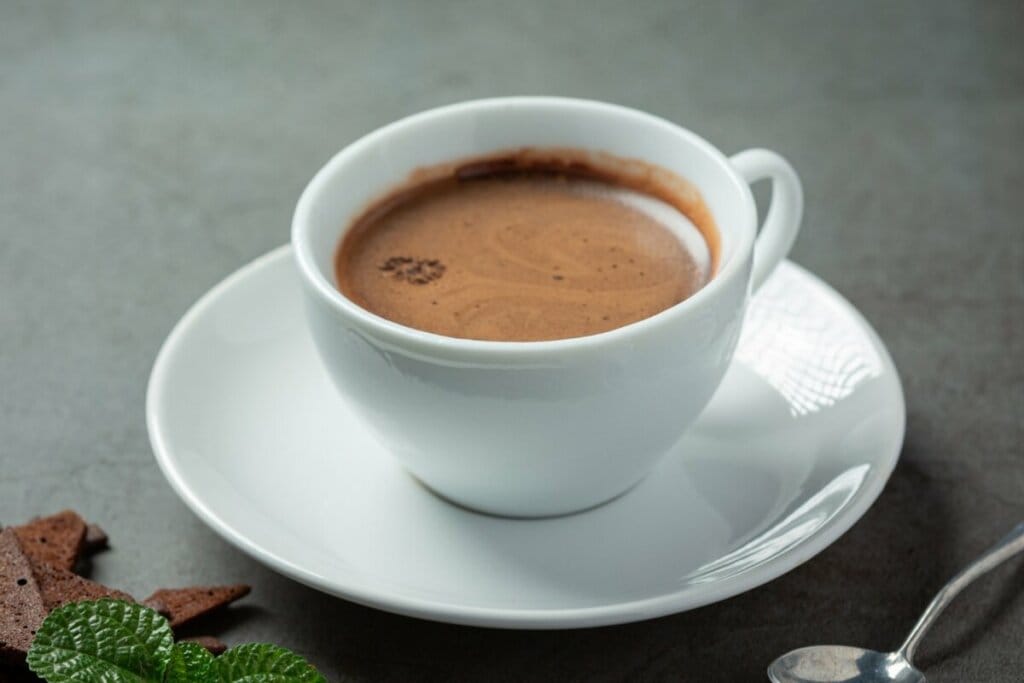 Xícara branca com chocolate quente em cima de uma mesa
