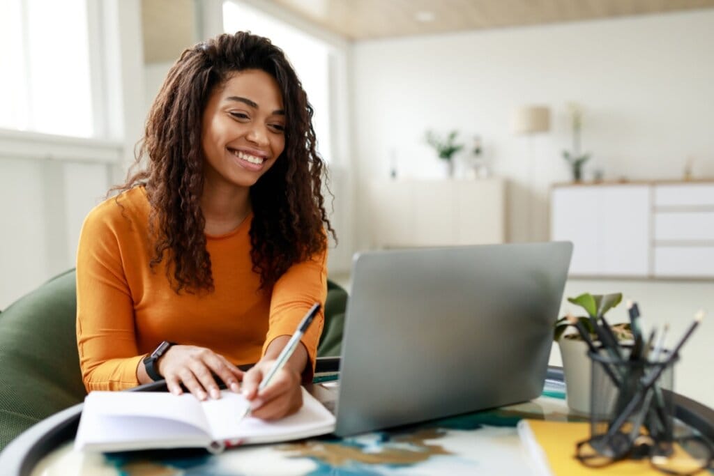 Jovem com cabelo cacheado solto e longo, usando suéter laranja conferindo resultado de simulado