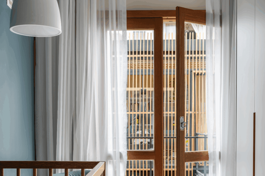 Porta de madeira com vidro em sacada de quarto com cortina branca