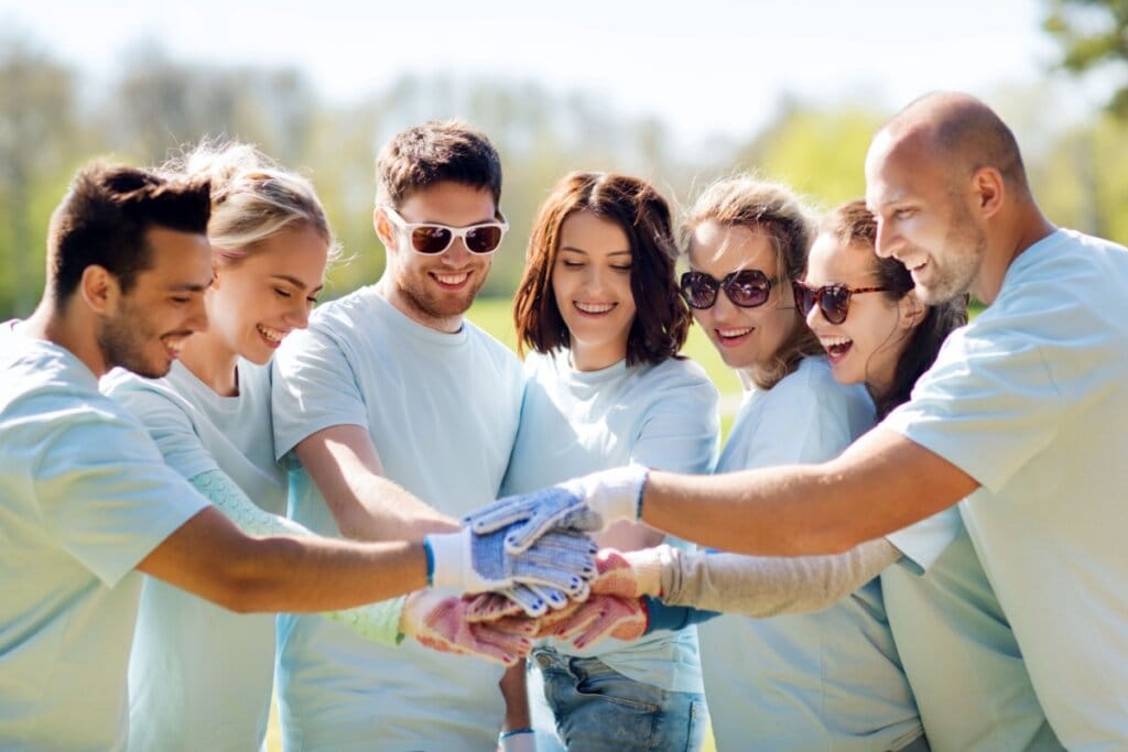 Grupo de pessoas usando camiseta azul clara juntando as mãos e sorrindo