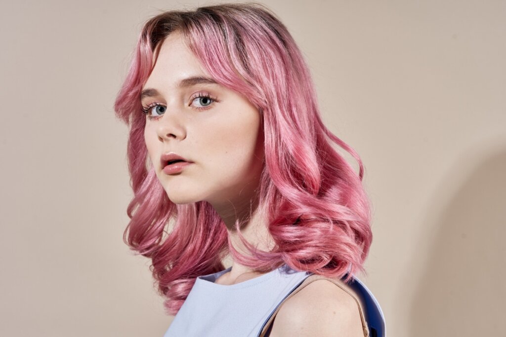 Mulher com cabelo rosa e franja posando para uma foto em frente a um fundo bege