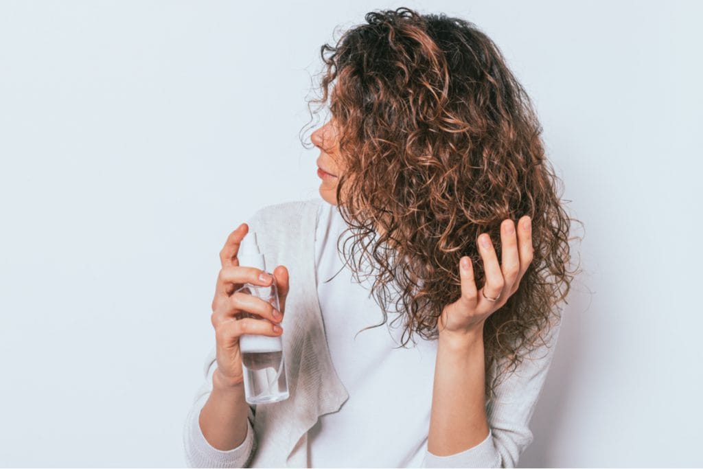 Mulher fazendo finalização no cabelo ondulado com um spray