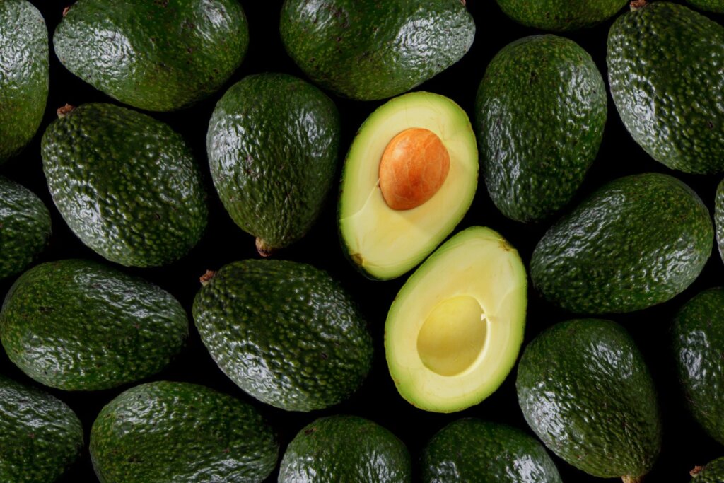 diversos abacates juntos com casca verde. abacate partido ao meio em cima deles