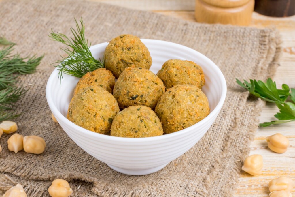 Bolinho de grão-de-bico servido em tigela branca em cima de toalha de mesa bege em cima de mesa de madeira