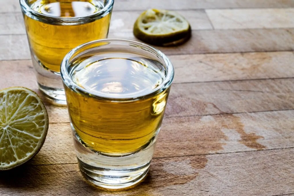 Cachaça marrom em dois copos de vidro com rodelas de limão ao lado 