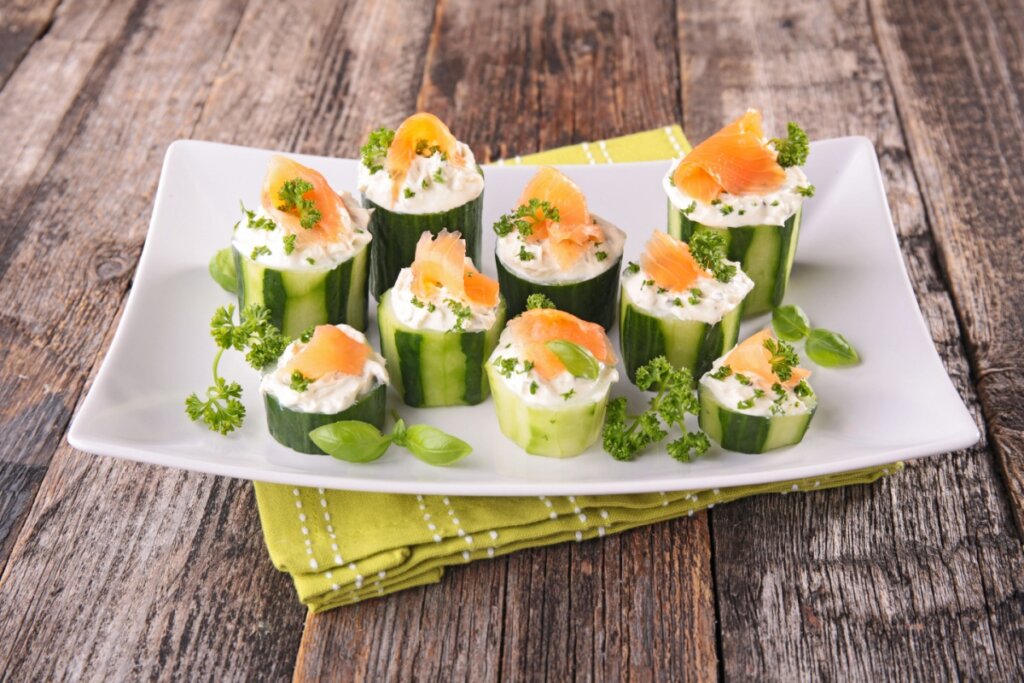 Canapés de pepino em cima de um prato branco com creme branco e tiras de salmão defumado 