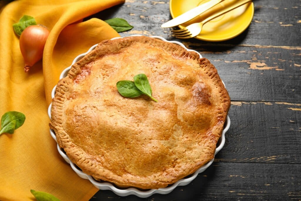 Empadão em uma travessa branca sobre uma mesa de madeira com pano amarelo