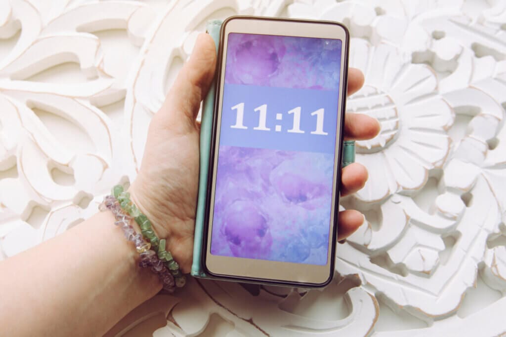 mão segurando celular mostrando 11:11 na tela com fundo roxo