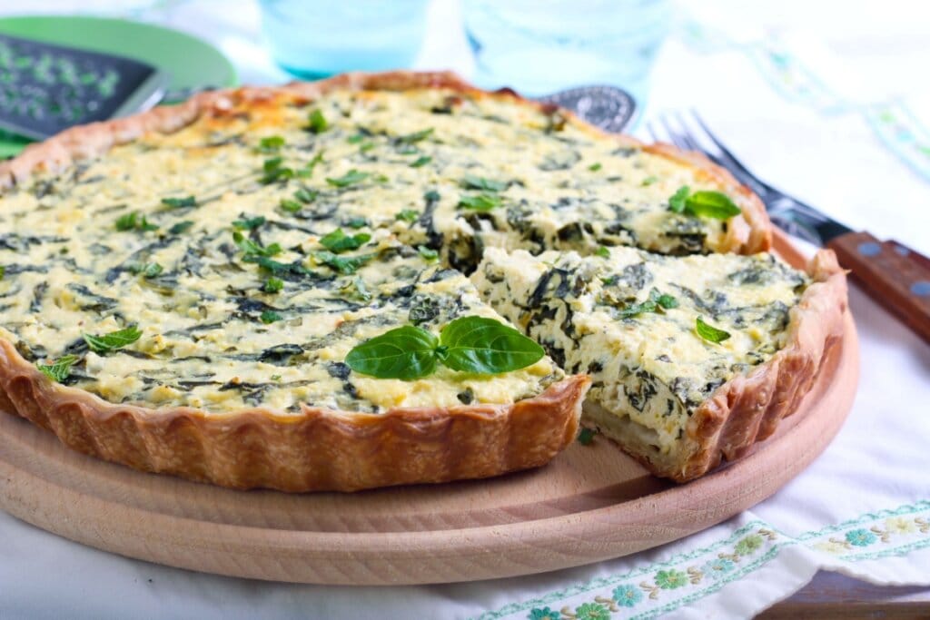 Quiche de espinafre e queijo feta servido em tabua de madeira em cima de mesa de madeira