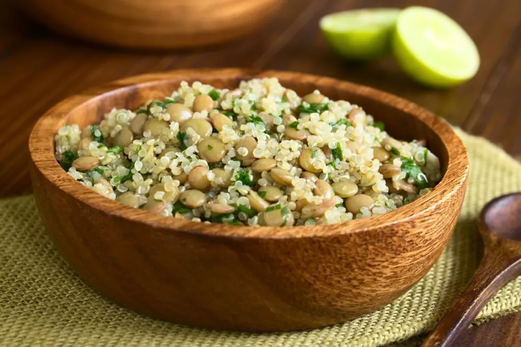 Salada morna de quinoa com lentilhas servido em tigela de madeira em cima de jogo americano verde em cima de mesa de madeira